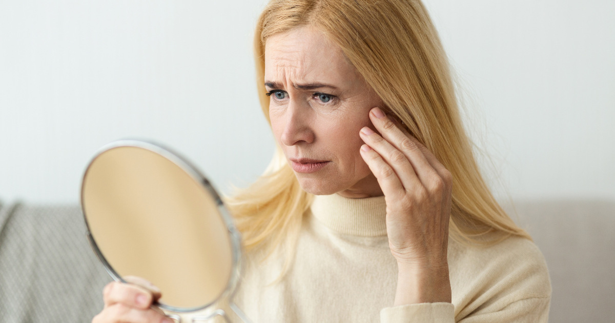 image of a middle aged woman looking at her skin in the mirror