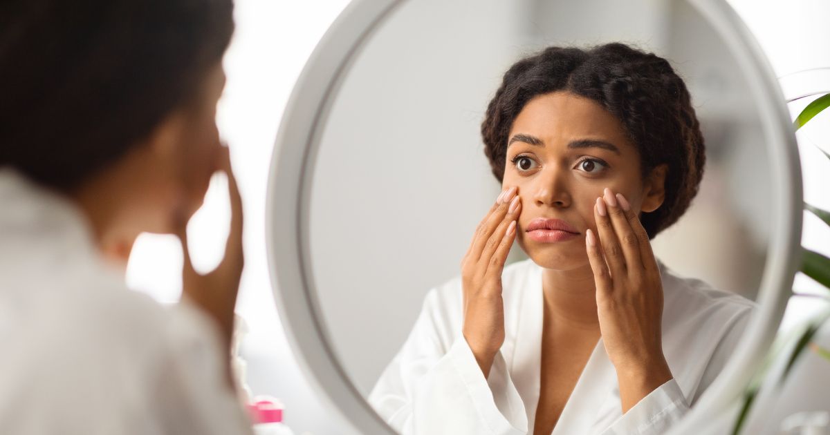 woman with darker skin looking in a mirror at their skin